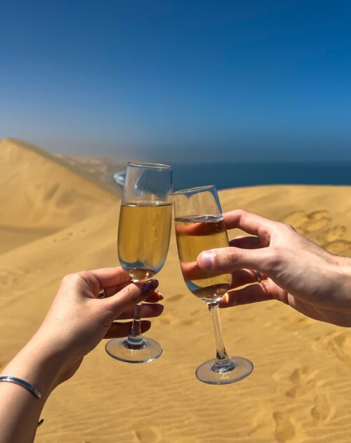 Show full-screen, Young couple clink glasses with champagne. Sandwich Harbour in Namibia at coast